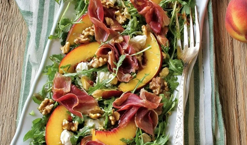 Insalata di pesche, rucola e bresaola servita in un piatto elegante.