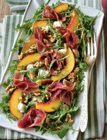 Insalata di pesche, rucola e bresaola servita in un piatto elegante.