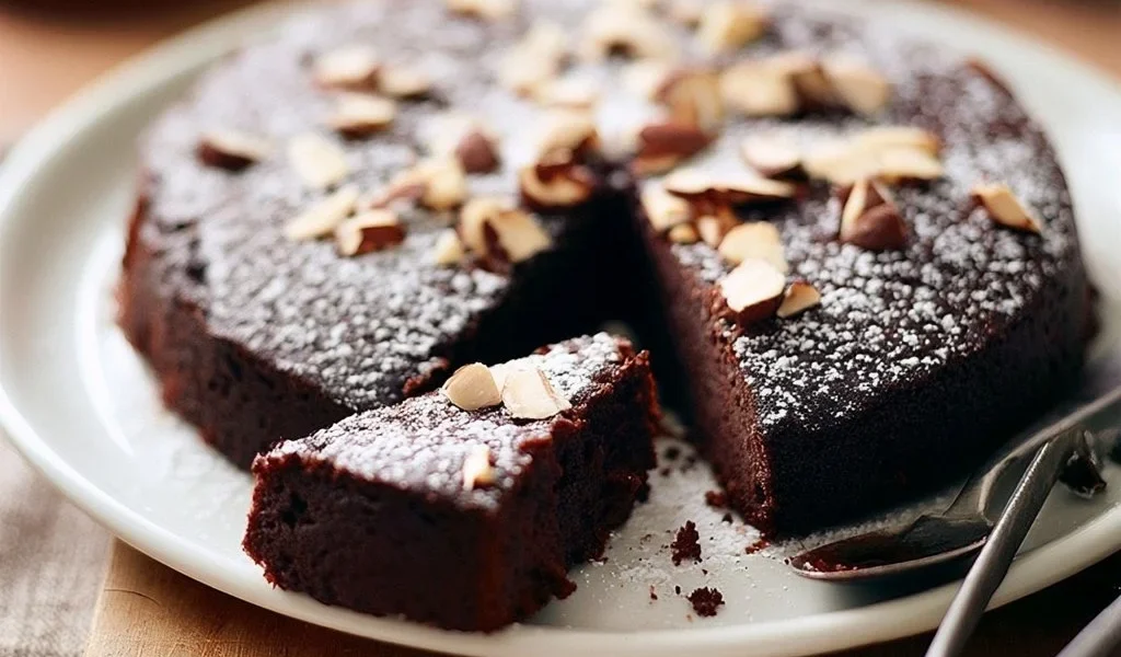 Torta umida al cioccolato fondente e mandorle su piatto decorativo.