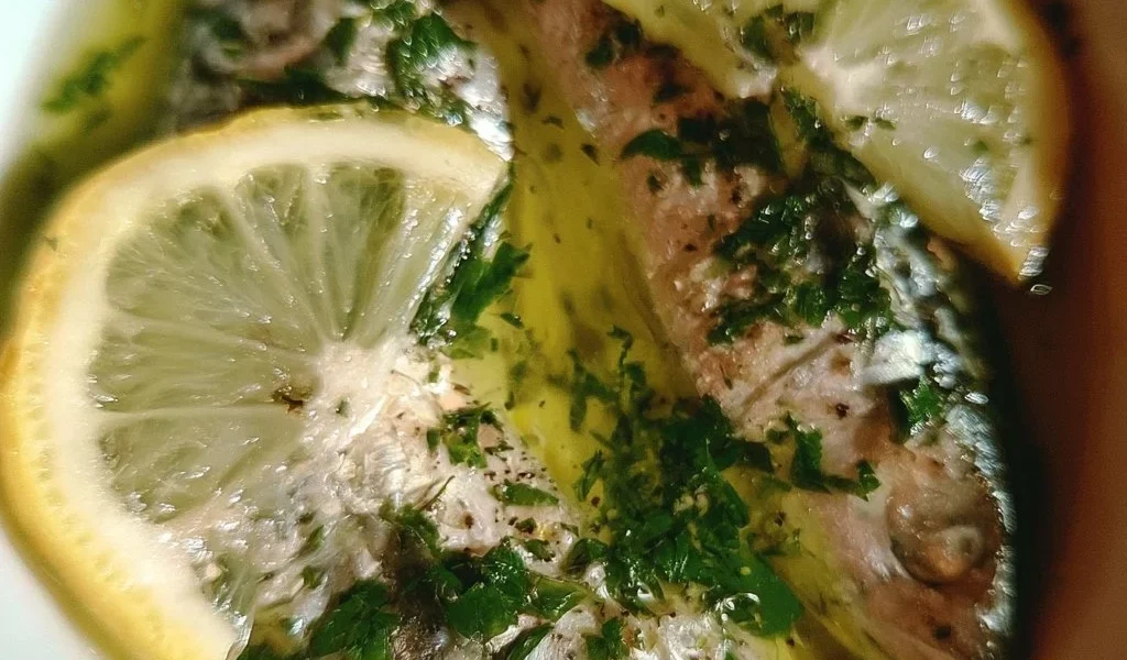 Sgombro cucinato con olio, limone e prezzemolo, servito su un piatto elegante.