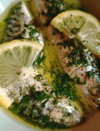 Sgombro cucinato con olio, limone e prezzemolo, servito su un piatto elegante.