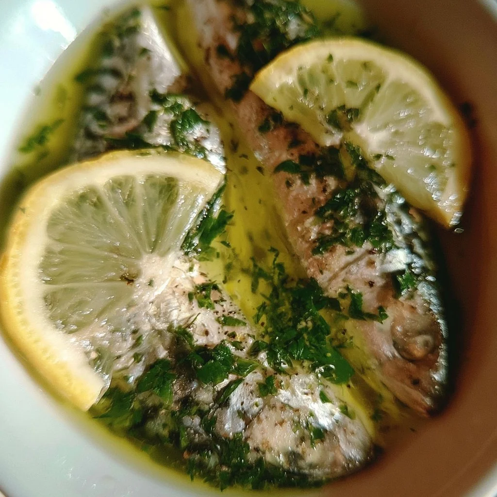 Sgombro cucinato con olio, limone e prezzemolo, servito su un piatto elegante.