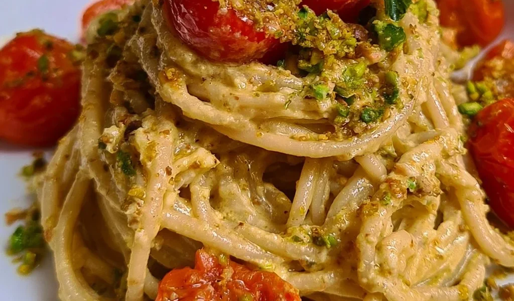 Spaghetti crema di ricotta con pistacchi e pomodorini in un piatto gustoso