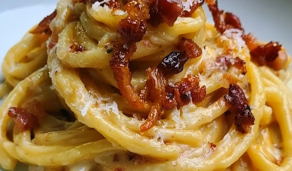 Spaghettoni con crema di patate, pecorino e guanciale serviti in un piatto elegante.