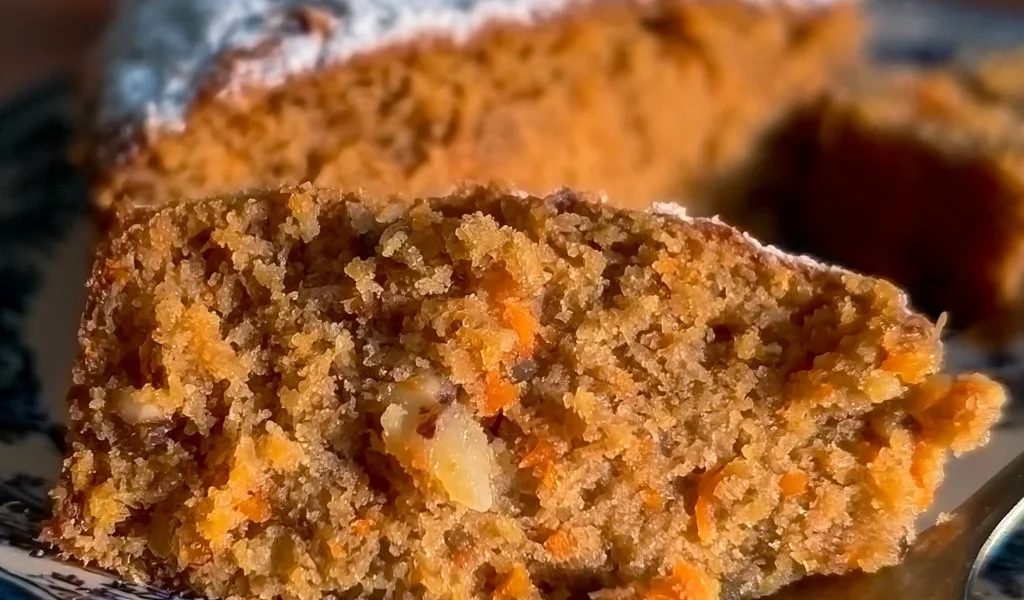 Fetta di torta di carote con crema frosting su un piatto.